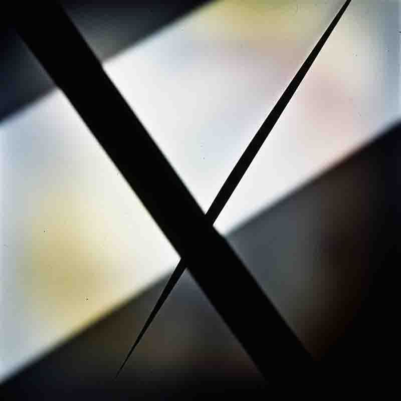 Abstrakte Farbfotografie, die eine starke geometrische Komposition zeigt, dominiert von zwei scharfen, dicken, schwarzen Diagonalen, die sich in einer X-Form kreuzen.